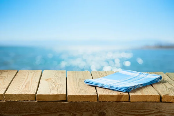 Empty wooden table with tablecloth over sea beach background — Stock Photo, Image