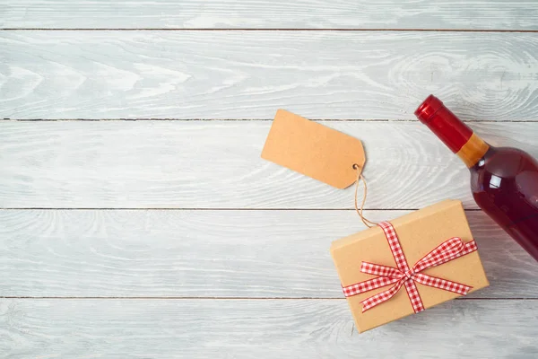 Gift box, bottle of wine and gift tag on wooden table background