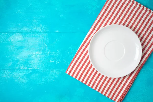 Beyaz boş plaka ve mavi ahşap arka kırmızı çizgili masa örtüsü — Stok fotoğraf