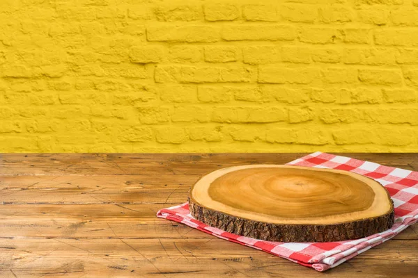 Leerer Holztisch mit Tischdecke und Holzbrett über gelb — Stockfoto