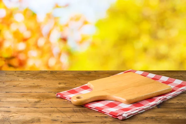 Empty wooden table with cutting board and tablecloth over autumn — Stock Photo, Image