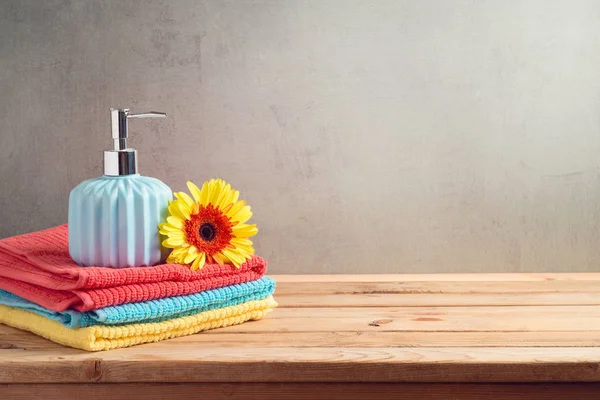 Bath towels and soap bottle on wooden table over bathroom wall b — Stock Photo, Image