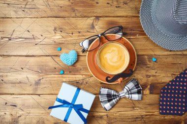 Kahve fincanı, bıyık, şapka, kravat ve tahta masadaki hediye kutusuyla Babalar Günü konseptin kutlu olsun. Yukarıdan üst görünüm