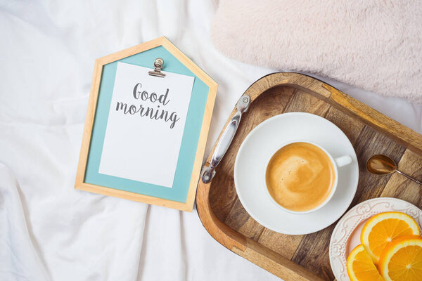 Coffee cup and fresh oranges on wooden tray on morning bed background. Top view from above