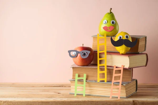 Back to school concept with books, funny cute apple, lemon and pear on wooden table