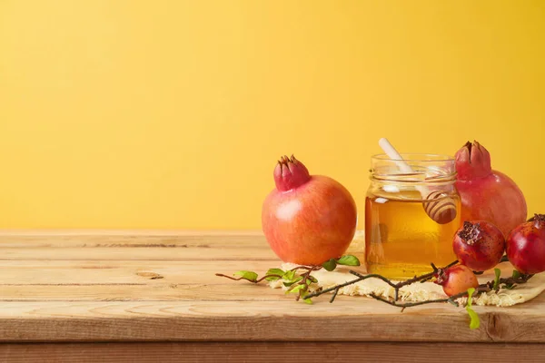 犹太假日Rosh Hashanah的概念 将蜂蜜罐和石榴放在黄色背景的木制桌子上 — 图库照片