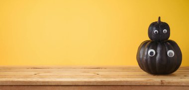 Sarı arka planda Cadılar Bayramı siyah balkabağı dekoru olan boş tahta masa