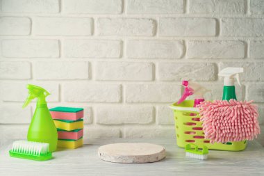 Boş ahşap podyum, temizlik şişeleri ve malzeme beyaz ahşap masa üzerine tuğla duvar arka planı. Bahar temizliği ürün gösterimi için hazırlanıyor.