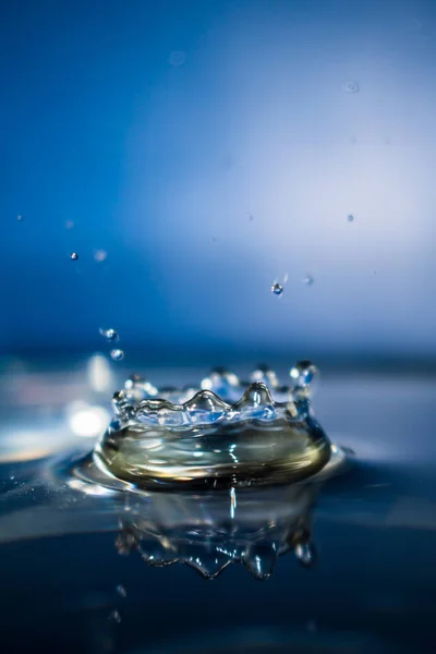 Macro shot of a water droplet impacting. Water splashing as it falls on surface of clear water, droplets spraying, with a blue background