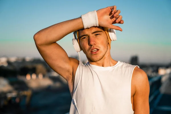 Tired athlete wiping sweat with his hand while wearing headphones