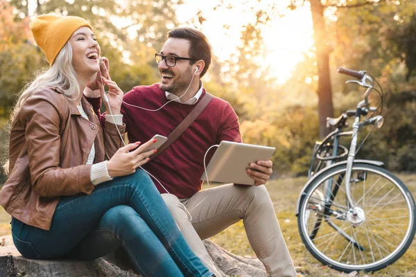 Playful young couple listening to music while holding tablet and smartphone in the citty park