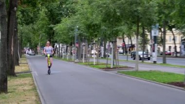 Viyana - 11 Temmuz 2019: Sarışın bir kadın Avusturya, Viyana 'da bisiklet pisti boyunca kiralık bir elektrikli scooter kullanıyor.