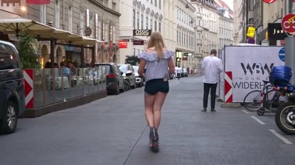 ウィーン 2019年7月11日 ショートパンツの後ろポケットにスマートフォンを持つブロンドの女性が オーストリアのウィーンの通りにレンタル電動スクーターに乗っています — ストック動画