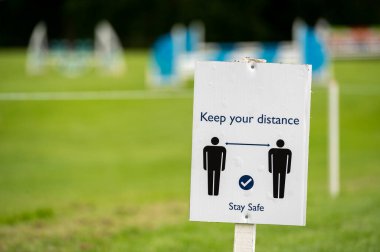 Arka planda odaklı olmayan bir açık hava olayı ile Covid-19 sosyal uzaklık işareti.