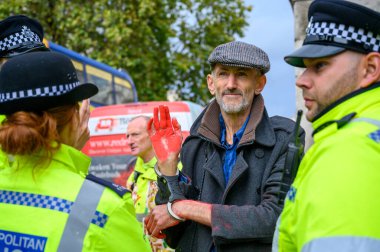 18 Ekim 2019: Elleri kırmızı boyalı, elleri polis memurları tarafından çevrili, elleri kelepçeli, erkek soykırımcı protestocu