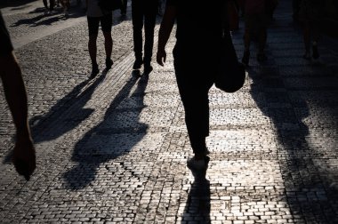 Tek renkli, siluetli bacaklar ve uzun gölgeler gecenin erken saatlerinde eski bir kaldırımlı caddede güneş ışığı altında..