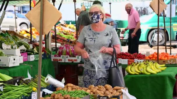 英国ノースヨークシャー州リッチモンド2020年8月1日 屋外の果物や野菜の市場の屋台でジャガイモのための装飾的な保護顔マスクとショッピングを身に着けている熟女 — ストック動画