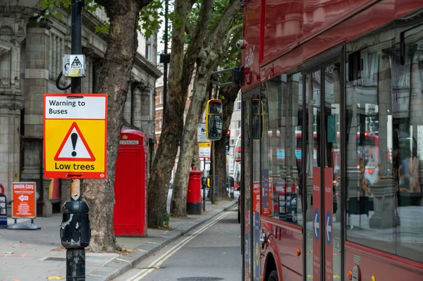 2020年9月12日 一辆红色伦敦双层巴士旁边的低矮树警告标志和背景中的旧电话亭和邮筒 — 图库照片
