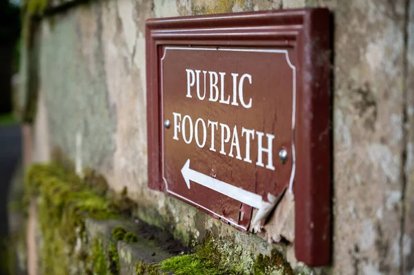 Close up view of an old distressed Public Footpath sign on a moss covered old stone wall.