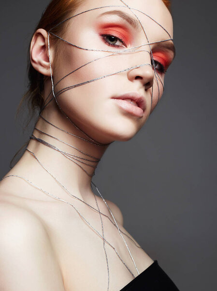Fashion portrait of beauty make-up girl with orange eye shadow. Beautiful young Woman with makeup and silver thread on the face and Body