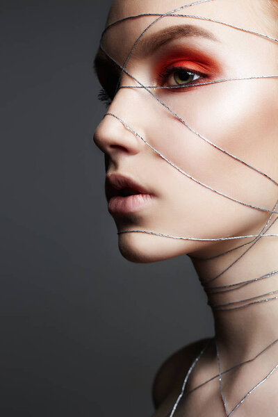 beauty make-up girl with orange eye shadow. Beautiful young Woman with makeup and silver thread on the face and Body