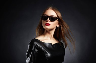 Güzel genç kadın güneş gözlüğü ve deri elbise. Moda güzellik sağlıklı saçlar uçan kız, kırmızı ruj,