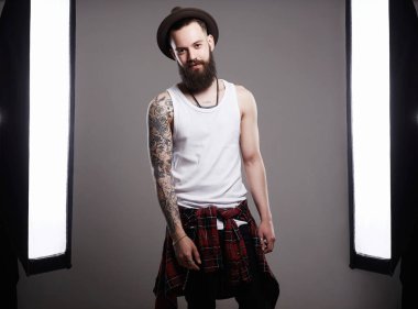 Moda Photosession şapkalı yakışıklı sakallı adam. Acımasız hipster çocuk dövme bir fotoğraf stüdyosunda poz ile