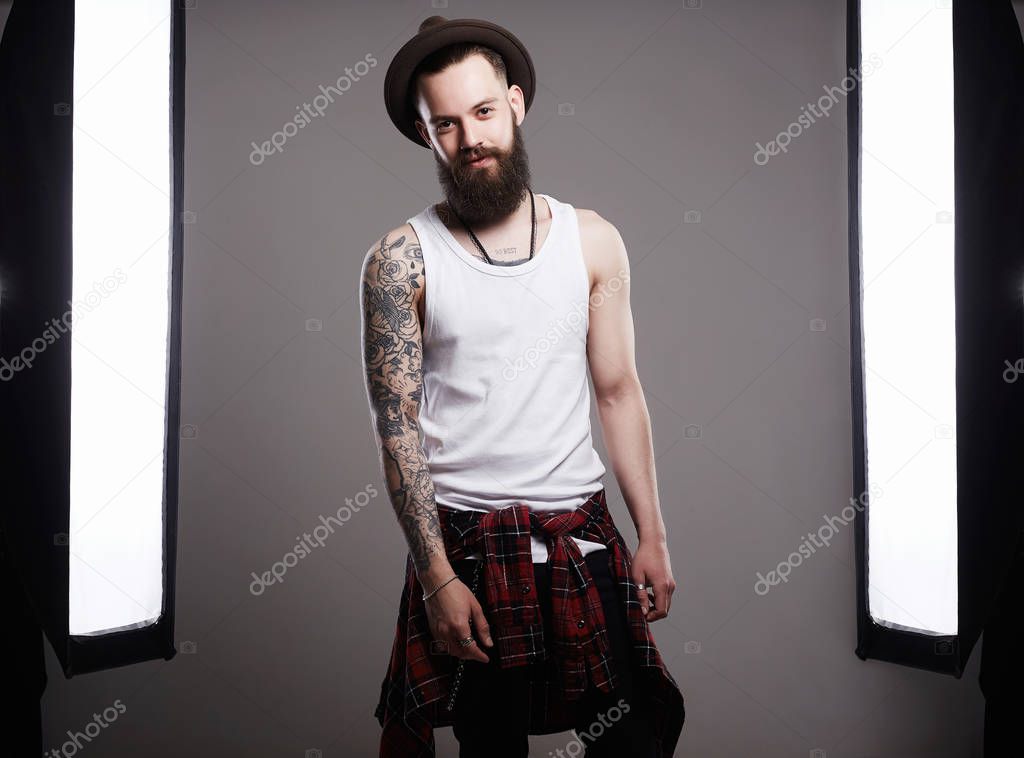 Fashion Photosession of Handsome Bearded Man in Hat. Brutal hipster boy with tattoo posing in a photo studio