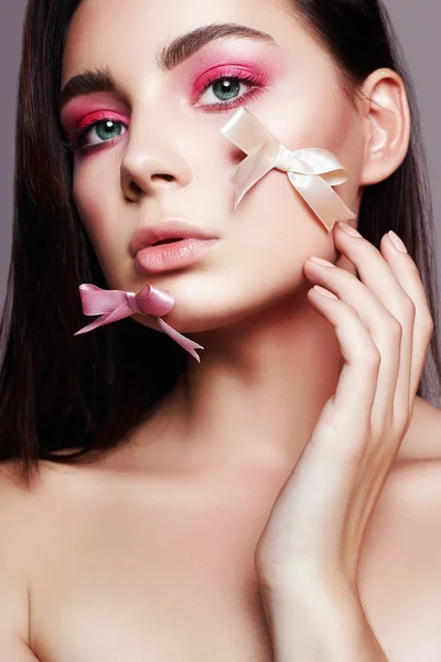 Sensual Beautiful Girl with makeup and silk bow on the face. beauty make-up girl with pink eye shadow. young Woman