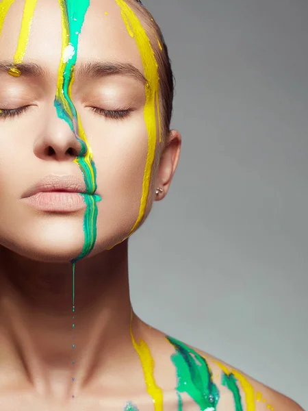 Young woman in Yellow and blue paint. liquid paint flowing over a beautiful face and Body. Color portrait of Girl in Paint