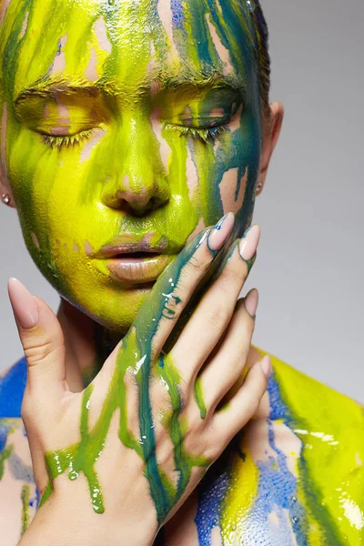 Young woman in paint. liquid paint flowing over a beautiful face and Body. Color close-up portrait of Girl in Paint