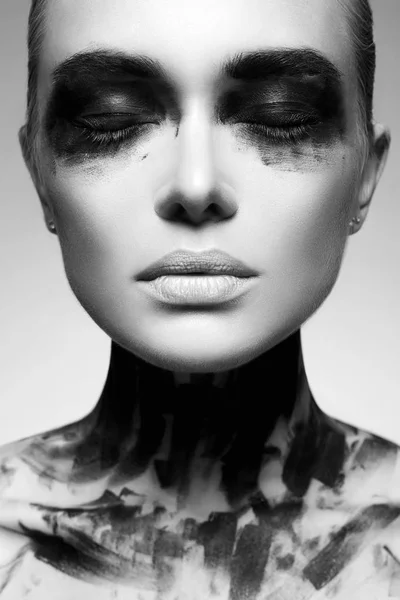 Black and white portrait of Beautiful Young woman with Dirty Paint Face. paint over a face and Body. Girl in Black Paint