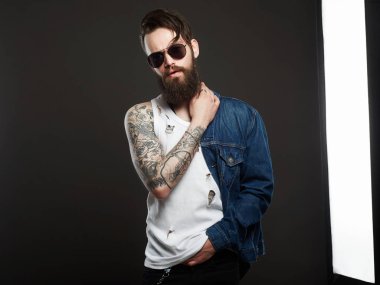 dövme ve güneş gözlüğü moda yakışıklı adam. Hipster sakallı şık çocuk kot pantolon ve gözlük