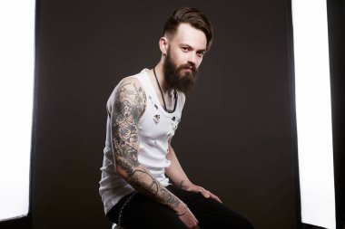 Photo studio poz sakallı adam. yakışıklı Brutal hipster vintage yırtık kirli gömlekli sakallı. Şık saç kesimi ve dövme bir çocuk