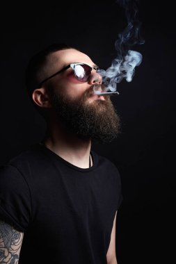 yakışıklı Brutal yasaktır erkek güneş gözlüğü sakallı. Hipster tattoed çocuk sigara ile