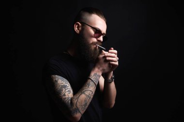 adam bir sigara yakıyor. yakışıklı Brutal yasaktır erkek güneş gözlüğü sakallı. Hipster tattoed çocuk