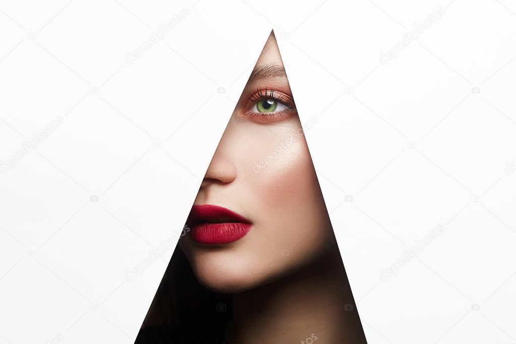 young beautiful woman with a bright makeup. make-up artist concept. A girl with beautiful bright green eyes with shining shadows, looks into the hole of white paper