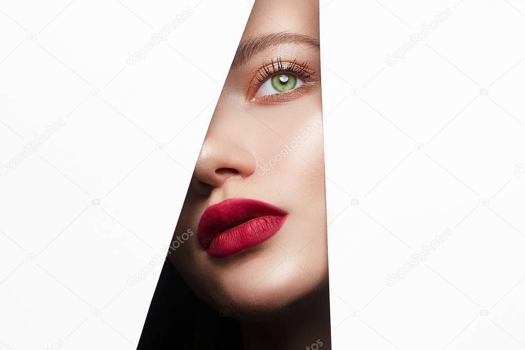 beautiful woman with a makeup, looks into the hole of white paper. make-up artist concept. A girl with beautiful bright green eyes and red Lips