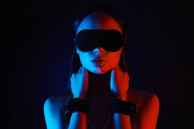 Kelepçeli ve maskeli bir kız. Renkli ışıklarda güzel bir kadın. Sanat tasarımı, parlak vücutlu renkli bir kız. Elleri bağlı ve gözleri bağlı bir kadın