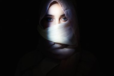 Tesettürlü genç ve güzel bir kadın, karanlıktan bakıyor. Kapüşonlu güzel kız. moda doğulu kadın