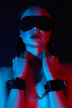 Kelepçeli ve maskeli bir kız. Renkli ışıklarda güzel bir kadın. Sanat tasarımı, parlak vücutlu renkli bir kız. Elleri bağlı ve gözleri bağlı model