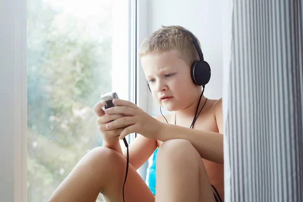 小男孩在玩一个游戏或者用耳机用智能手机听音乐 家中儿童的生活方式肖像 — 图库照片