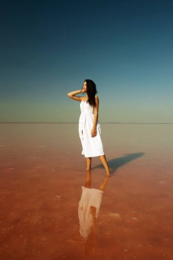 Pembe tuz gölünde suyun üzerinde duran beyaz elbiseli güzel kız. gün batımı