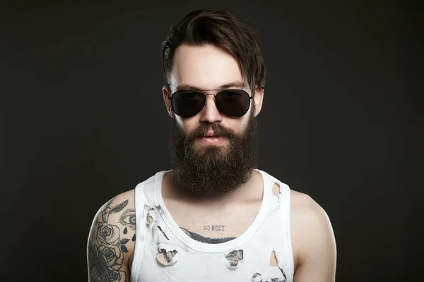 handsome tattooed man in sunglasses. Brutal bearded hipster boy in glasses and vintage torn dirty shirt