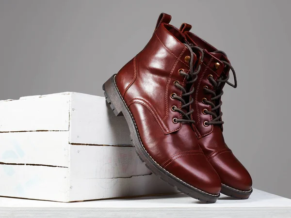 Trendy mans red boots on white wooden box. fashion shoes still life