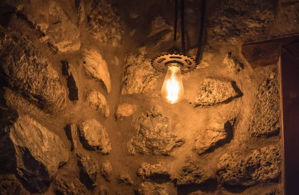 yellow light bulb hanging from chains next to an old stone wall inside an old building