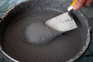 Elinde malayla beton alçılı bir kovada çalışan bir işçi.