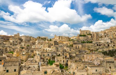 Sassi di Matera tarihi panoramik manzaralı Sasso Caveoso kaya mağara evlerin önünde mavi gökyüzü ve beyaz bulutlar, Unesco Dünya Mirası, Basilicata, Güney İtalya eski antik şehrin merkezi