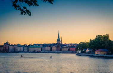 Old historical town quarter Gamla Stan with traditional typical buildings with colorful walls, park of Skeppsholmen island, jet ski and boat on Lake Malaren water at sunset, Stockholm, Sweden clipart