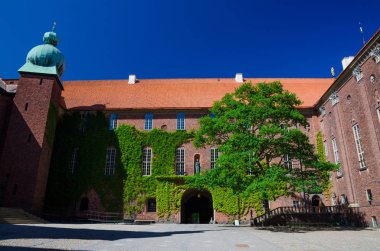 Avlu içinde Stockholm City Hall (Stadshuset) Nobel Ödülü ziyafet mahkemelerinin ve Belediye Meclisi Ivy ile bina tuğla duvarlar, döşenmiş çatı, mavi gökyüzü, İsveç ile insanlar yürüyen yeşil ağaç kaplı.